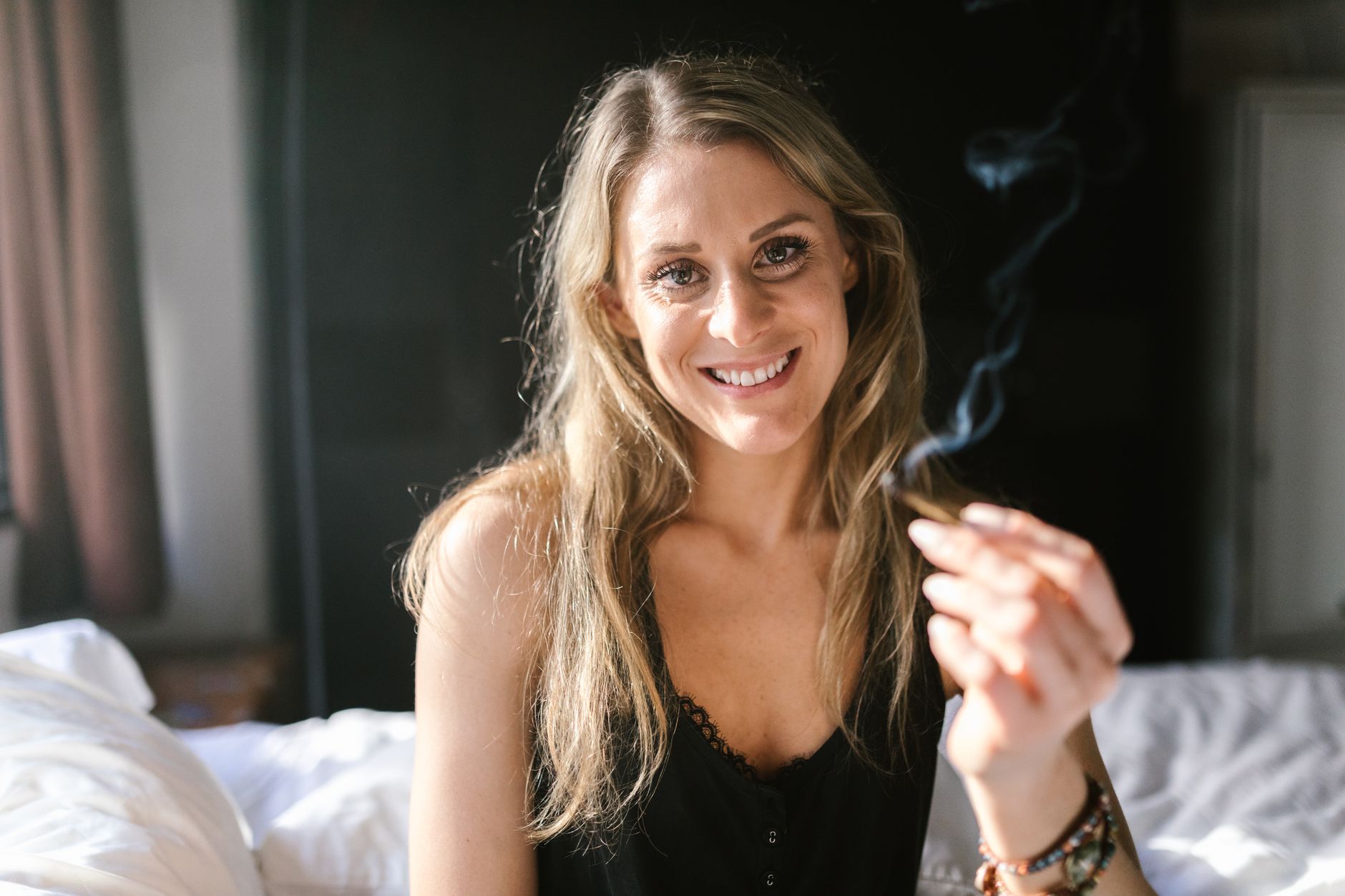 Lächelnde Frau hält einen Joint und verkörpert entspannte Cannabiskultur in einem Innenraum.