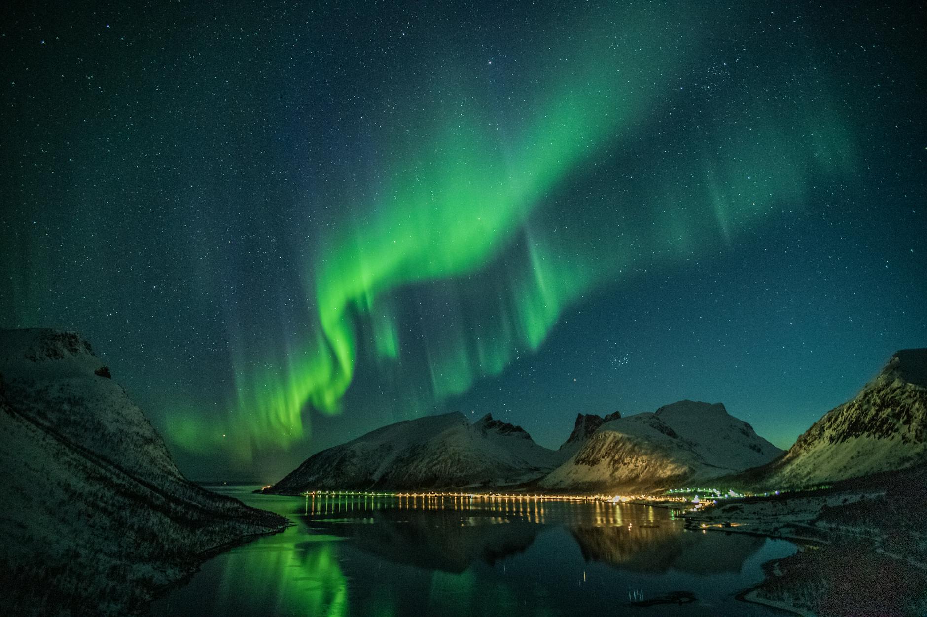 Faszinierende Nordlichter über schneebedeckten Bergen, im ruhigen See reflektiert, unter einem Sternenhimmel.
